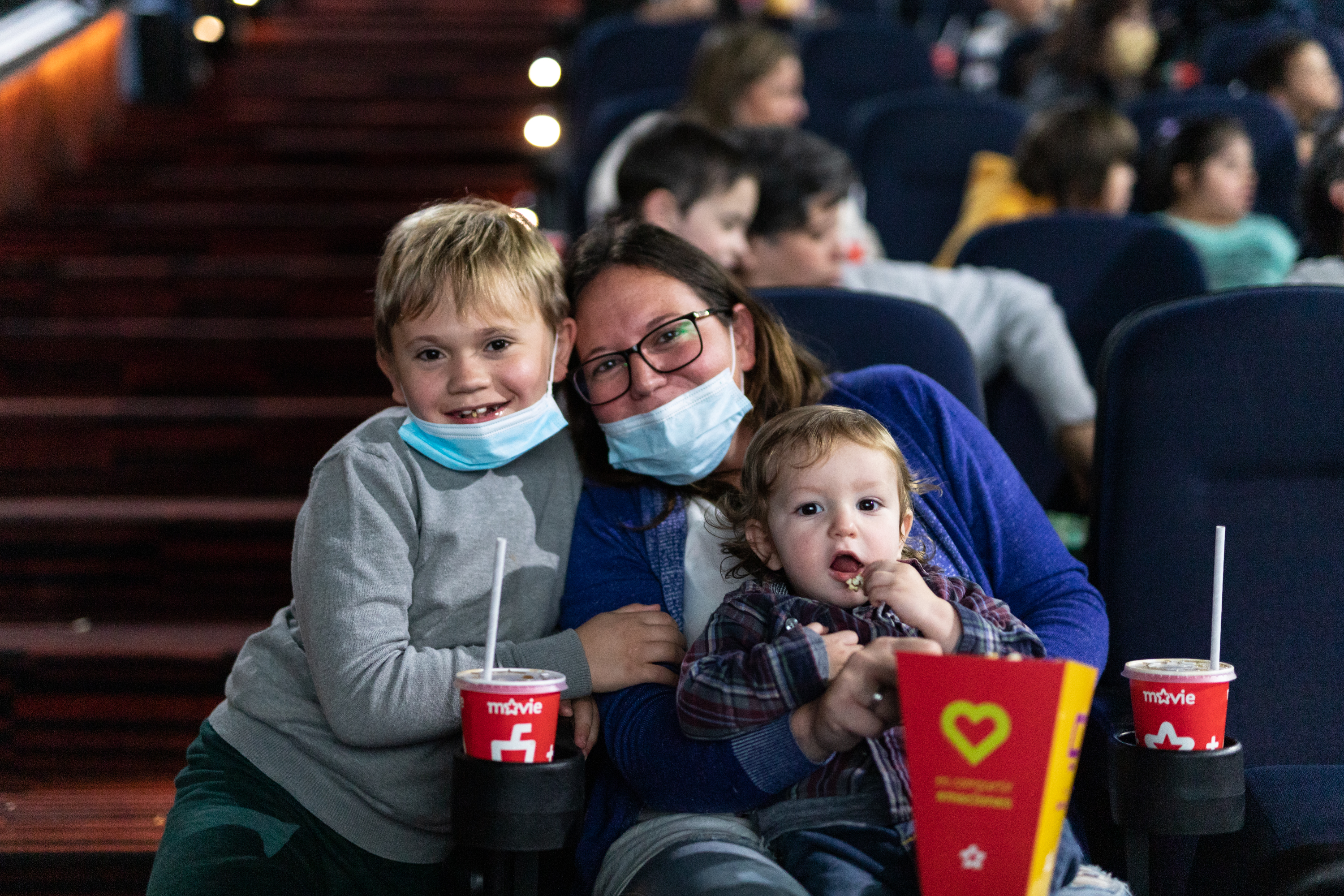 Dentro del cine, una madre disfruta de la película junto a sus dos hijos.